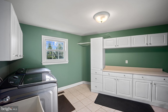 clothes washing area with washer and dryer, baseboards, light tile patterned flooring, and cabinet space