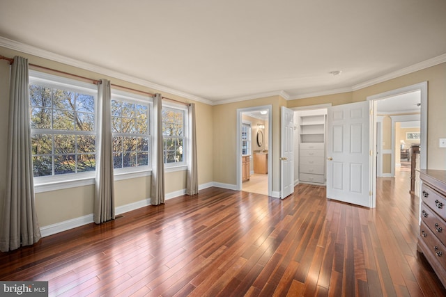 unfurnished bedroom with crown molding, dark wood-style flooring, baseboards, and a walk in closet