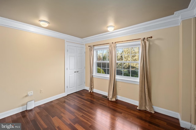 unfurnished bedroom with dark wood-type flooring, ornamental molding, baseboards, and a closet