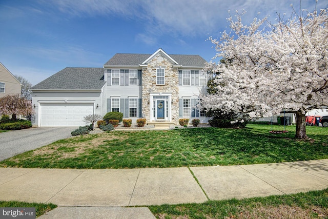 24 W Shakespeare Dr, Middletown, DE 19709 - colonial home featuring stone siding, a front yard, driveway, a garage, and roof with shingles