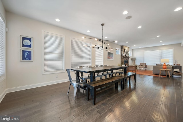 dining space featuring a stone fireplace, dark wood-style floors, baseboards, recessed lighting, and an inviting chandelier