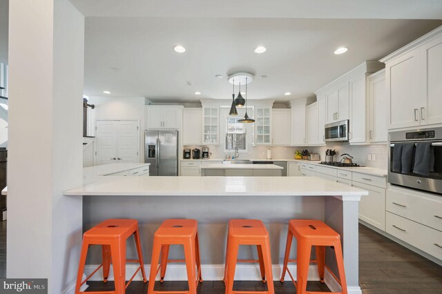 kitchen with white cabinets, a kitchen bar, appliances with stainless steel finishes, and glass insert cabinets