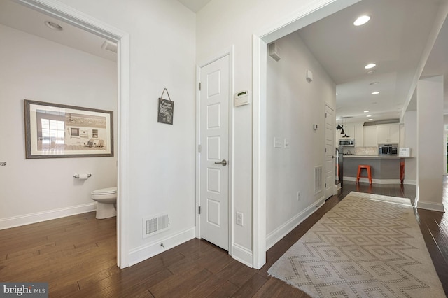 hallway with dark wood finished floors, baseboards, and visible vents