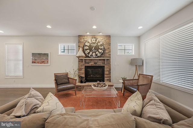 living area with a stone fireplace, baseboards, wood finished floors, and recessed lighting