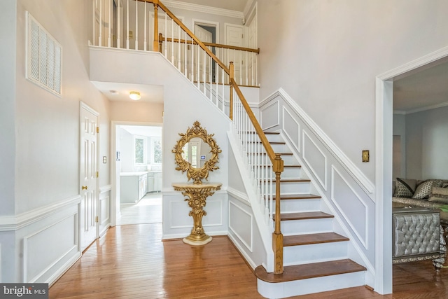 stairs with a towering ceiling, visible vents, wood finished floors, and a decorative wall