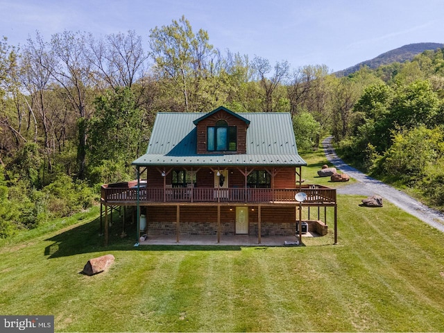 rear view of property featuring a lawn, a deck, a patio area, a view of trees, and stone siding