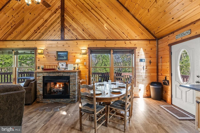 dining space with wooden walls, a healthy amount of sunlight, a stone fireplace, and lofted ceiling