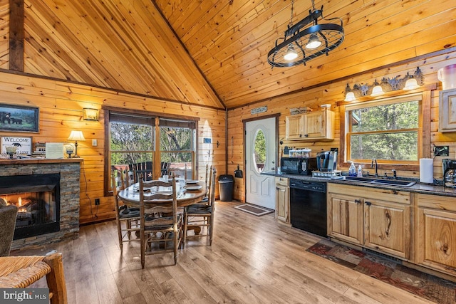 kitchen with dark countertops, light wood-type flooring, wood walls, a sink, and black appliances