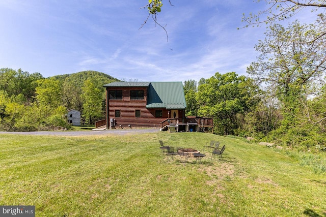back of house with a lawn, a wooden deck, an outdoor fire pit, and metal roof