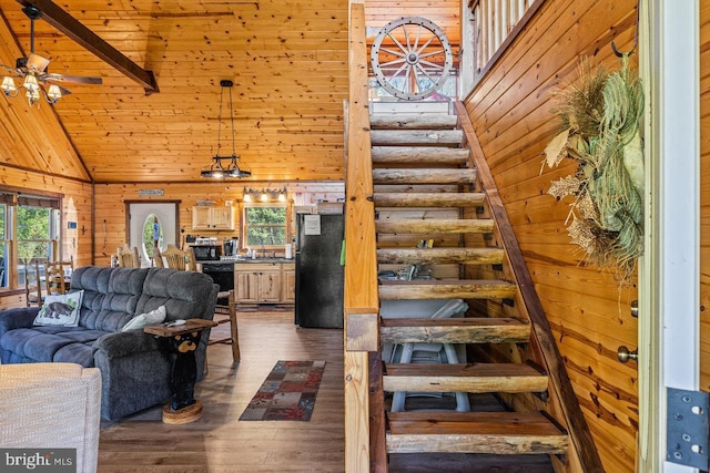 living room with dark wood-type flooring, stairs, wooden walls, and high vaulted ceiling
