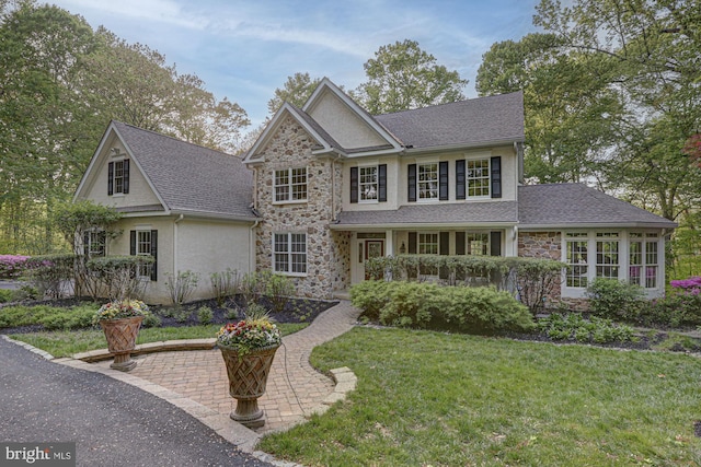 view of front of house with stone siding, a front lawn, and a shingled roof