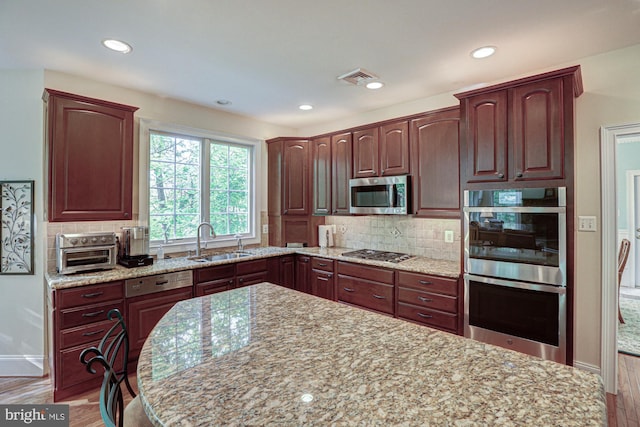 kitchen featuring appliances with stainless steel finishes, a sink, light wood-style flooring, light stone countertops, and recessed lighting