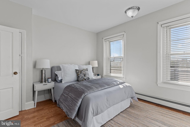 bedroom with a baseboard heating unit and wood finished floors