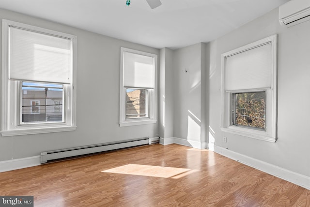 unfurnished room featuring baseboard heating, a wall mounted air conditioner, wood finished floors, and plenty of natural light