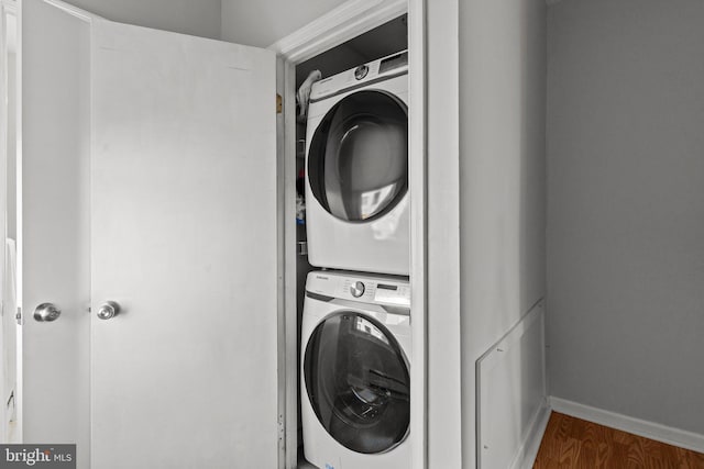 laundry room featuring baseboards, wood finished floors, stacked washer / dryer, and laundry area