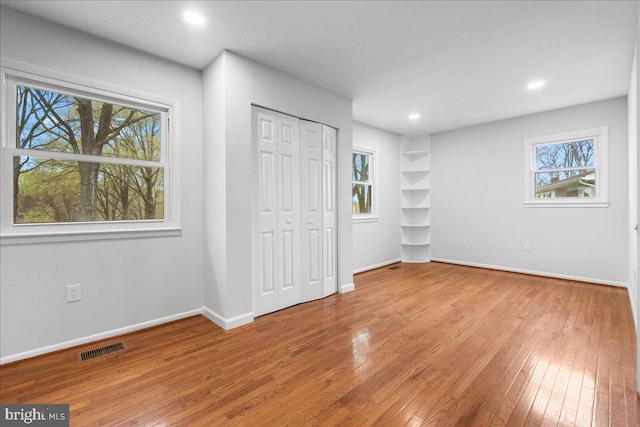 unfurnished bedroom with multiple windows, visible vents, and hardwood / wood-style floors