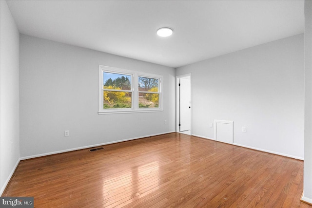 empty room with baseboards, visible vents, and wood finished floors