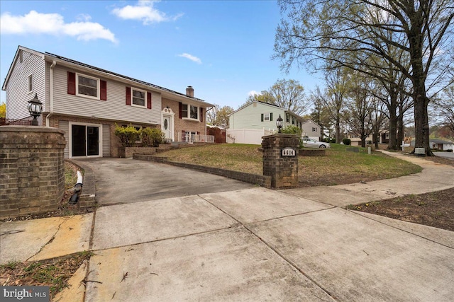 raised ranch with fence, a chimney, a front yard, brick siding, and driveway