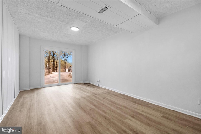 unfurnished room featuring wood finished floors, a textured ceiling, baseboards, and visible vents