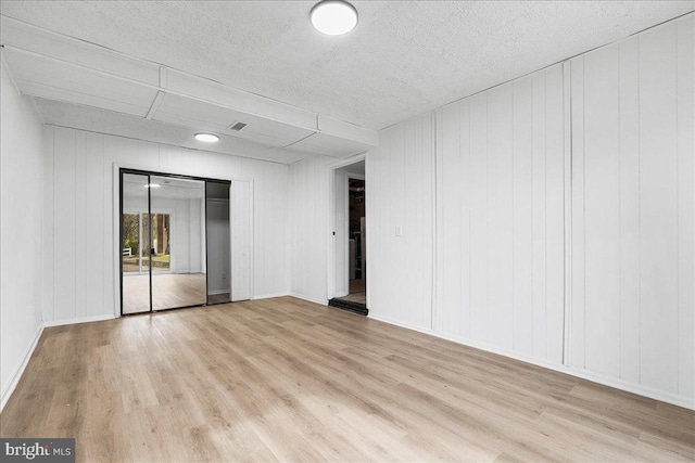 spare room with baseboards, light wood-style floors, and a textured ceiling