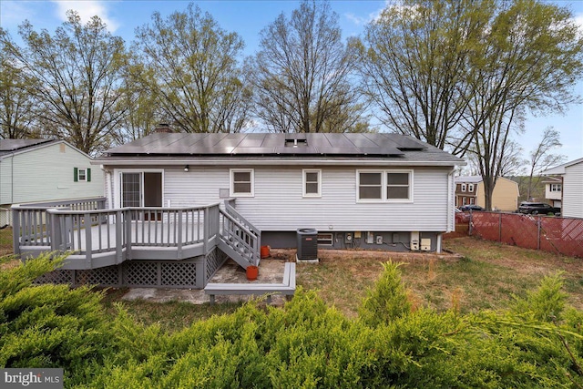 rear view of house featuring a chimney, central air condition unit, fence, a wooden deck, and roof mounted solar panels