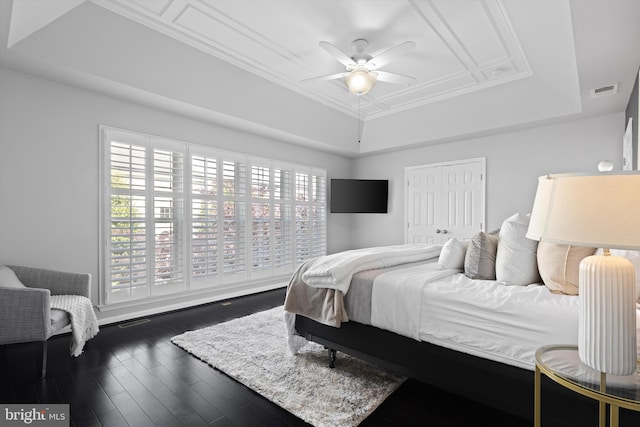 bedroom with a raised ceiling, dark wood finished floors, a closet, and ceiling fan