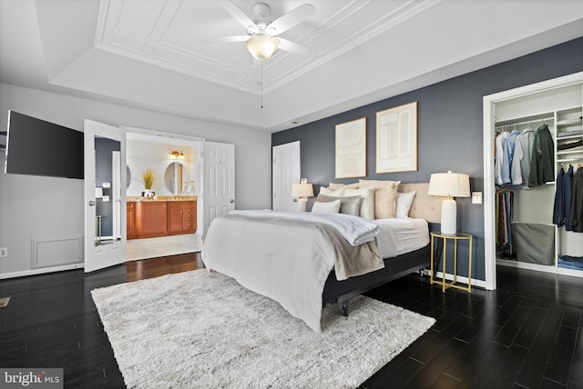 bedroom with a tray ceiling, dark wood-style floors, a walk in closet, a closet, and baseboards