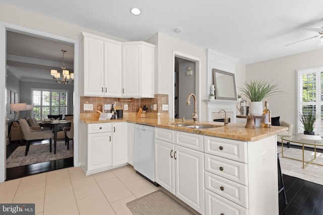 kitchen featuring white dishwasher, a sink, a chandelier, light stone counters, and plenty of natural light