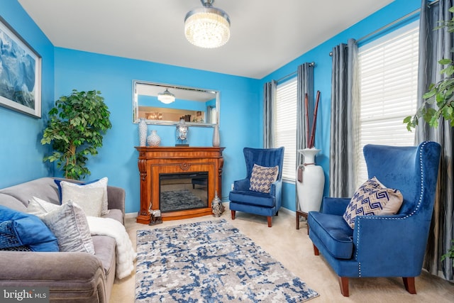 living area featuring a glass covered fireplace, a notable chandelier, baseboards, and carpet floors