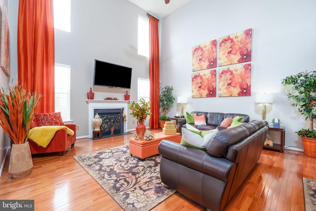 living room featuring a fireplace with flush hearth, a healthy amount of sunlight, a towering ceiling, and hardwood / wood-style flooring