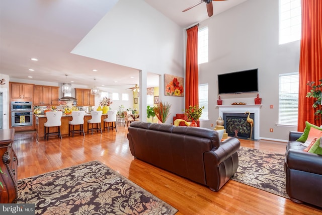 living room featuring a fireplace with flush hearth, a high ceiling, a ceiling fan, and plenty of natural light