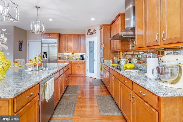 kitchen with wall chimney range hood, a chandelier, backsplash, appliances with stainless steel finishes, and a sink