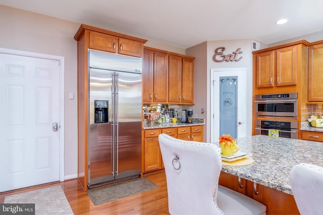 kitchen featuring light wood-style flooring, decorative backsplash, appliances with stainless steel finishes, and light stone countertops