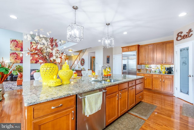 kitchen featuring an inviting chandelier, a sink, appliances with stainless steel finishes, light wood-style floors, and pendant lighting