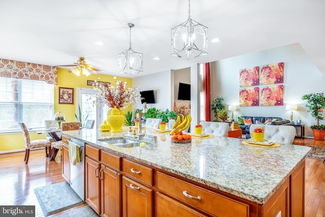 kitchen with ceiling fan with notable chandelier, stainless steel dishwasher, a sink, open floor plan, and a center island with sink