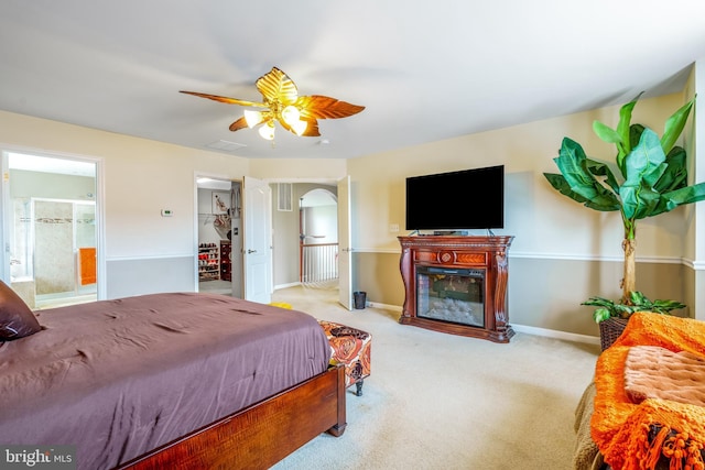 bedroom with a glass covered fireplace, baseboards, carpet flooring, connected bathroom, and ceiling fan