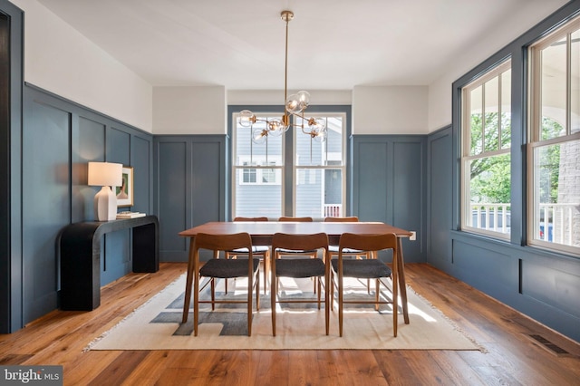 dining area featuring a decorative wall, a chandelier, a wainscoted wall, and wood finished floors