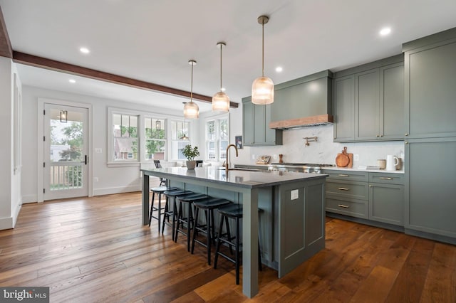 kitchen with wall chimney exhaust hood, tasteful backsplash, a kitchen island with sink, a kitchen bar, and recessed lighting