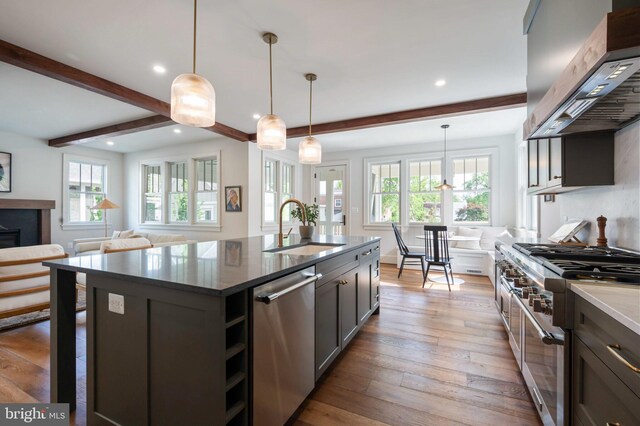 kitchen featuring stainless steel appliances, wall chimney range hood, a sink, recessed lighting, and beam ceiling