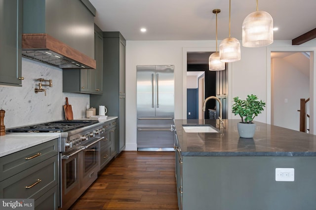 kitchen with premium appliances, premium range hood, a sink, dark wood-style flooring, and dark stone countertops