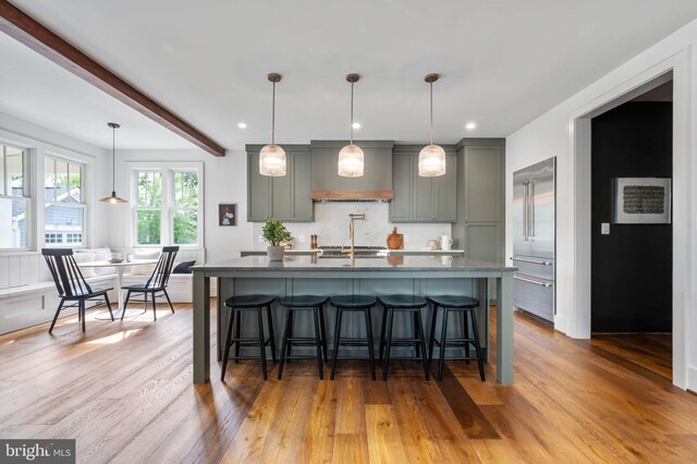 kitchen featuring wood finished floors, a breakfast bar, custom exhaust hood, a kitchen island with sink, and recessed lighting