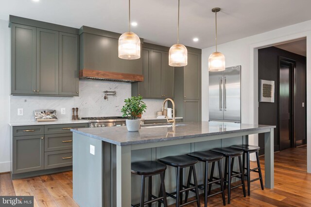 kitchen with built in fridge, a sink, backsplash, dark stone counters, and wood finished floors
