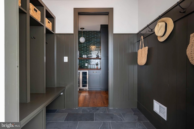 mudroom with wine cooler, wainscoting, bar, and dark tile patterned flooring