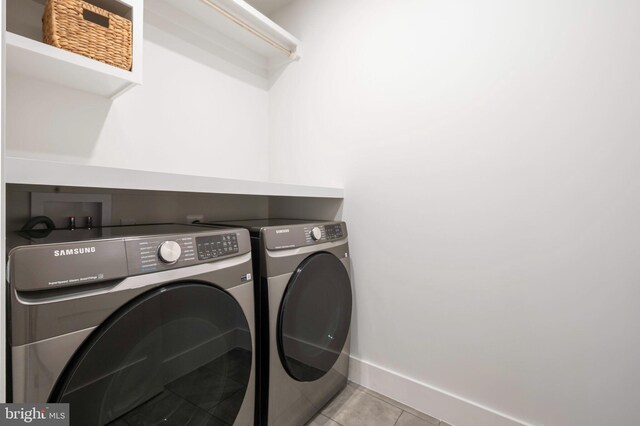 clothes washing area with washing machine and dryer, tile patterned floors, and baseboards