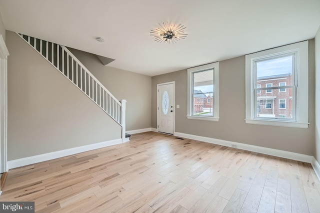 foyer entrance with baseboards, stairs, and light wood-style flooring