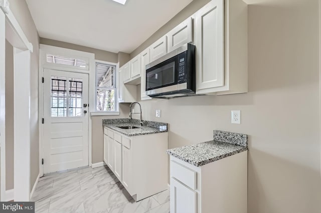 kitchen featuring stainless steel microwave, baseboards, marble finish floor, a sink, and light stone countertops