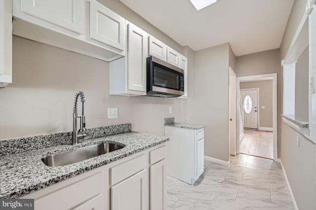 kitchen with stainless steel microwave, marble finish floor, a sink, and light stone counters
