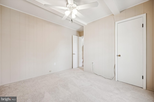 unfurnished bedroom featuring beamed ceiling, a ceiling fan, wood walls, and carpet
