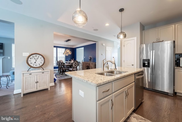 kitchen featuring light stone counters, dark wood-style floors, stainless steel appliances, a sink, and hanging light fixtures