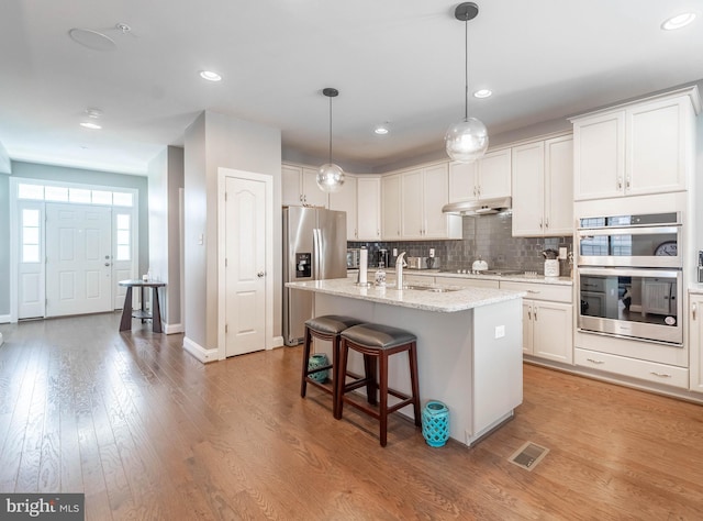 kitchen featuring light wood-type flooring, white cabinetry, backsplash, visible vents, and appliances with stainless steel finishes